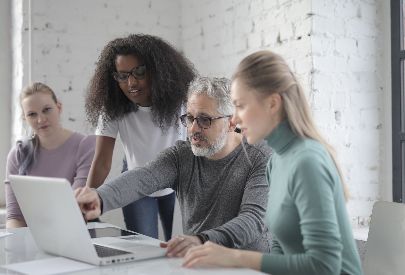 A team of four gathered around a laptop, working through something together